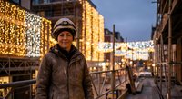 Middle-aged Caucasian man in winter clothing and knit hat smiling on festive city street with holiday lights and decorations during evening twilight hour.
