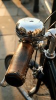 Vintage bicycle bell with weathered brown leather grip and polished chrome dome reflecting urban street scene, ideal for cycling, retro transport, and nostalgic design projects.