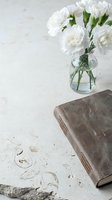 Vintage leather journal beside white carnations in a glass vase on a textured stone surface, evoking calm and mindful living.