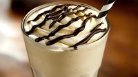 Creamy vanilla milkshake topped with chocolate syrup drizzle and striped straw, perfect for dessert menu photography or beverage advertising.