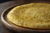 Freshly made golden crepe or thin pancake on rustic wooden plate, close-up view with soft natural lighting showing delicate texture and buttery surface.