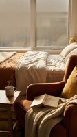 Cozy reading nook with armchair, coffee mug and open book by sunny window. Warm morning light creates peaceful atmosphere for relaxation and leisure time.