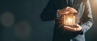 Businessman holding glowing house hologram in hands, representing real estate investment, property management, smart home technology, and digital innovation in housing sector.