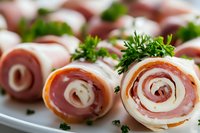 Ham and turkey roll ups garnished with fresh parsley on white plate, close up view of spiral deli meat appetizers for party or catering service.