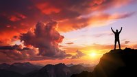 Man celebrating success on mountain peak at dramatic sunset with arms raised against colorful sky and clouds for motivation and achievement concepts.