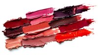 Lipstick smear swatches in various shades of red and pink on white background, showing texture and pigmentation of cosmetic products. Isolated makeup smudges.