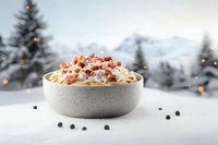 Creamy pasta carbonara with crispy bacon bits in ceramic bowl against snowy winter mountain landscape with pine trees.