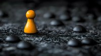 Orange wooden game piece stands alone among black pieces on dark textured surface, symbolizing leadership, uniqueness and standing out from crowd concept.
