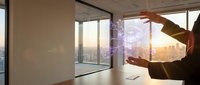 Businessman holding holographic digital interface in modern office with city skyline view at sunset showcasing future technology and innovation concepts.