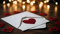 Love letter with red glitter heart on white envelope, surrounded by decorative hearts and warm bokeh lights, perfect for Valentine's Day, romance, and greeting card designs.