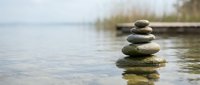 Zen stone stack balanced on calm lake water with blurred natural background for meditation wellness and mindfulness concepts.