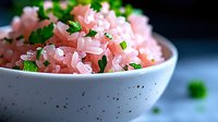 Pink pickled onions garnished with fresh herbs and sea salt in ceramic bowl on blue background, macro food photography highlighting vibrant colors and texture.