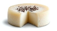 Creamy white chocolate cheesecake with slice removed showing smooth texture, topped with chocolate shavings on white background for dessert menu.