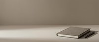 Stacked closed notebooks with blank covers on neutral beige surface with soft natural light, suitable for business, education, and stationery design projects.