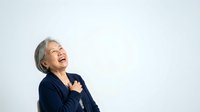 Senior woman with gray hair, wearing dark navy blazer, smiling joyfully while looking upward against white background. Suitable for business, healthcare, lifestyle and corporate projects.