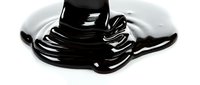 Thick black liquid dripping and pooling on white surface, creating glossy puddle with flowing streams and viscous texture for cosmetics, oil, or industrial product advertising.