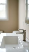 Modern stainless steel faucet with white ceramic sink in contemporary bathroom interior with natural light from windows, suitable for home decor and design projects.