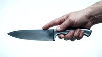Hand holding sharp kitchen knife with black handle isolated on white background for culinary cooking and food preparation concepts.