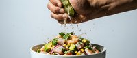 Male hand squeezing fresh lime juice over chickpea salad with vegetables in bowl against white background. Food preparation and healthy eating concept.
