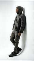 Young Black male model wearing dark hooded bomber jacket and cargo pants with black sneakers, standing in profile against white background for fashion and lifestyle campaigns.