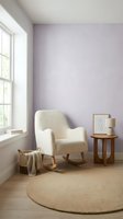 Serene reading nook with cream rocking chair, wooden side table, and framed botanical art against soft lavender wall near bright window for home decor.