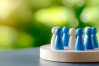 Blue and white game pieces arranged on wooden circular platform against blurred green background representing leadership, teamwork and business strategy.