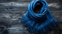 Cozy blue wool scarf with fringe tassels on dark rustic wooden background, winter fashion accessory styled for seasonal warmth and comfort.