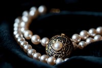 Elegant pearl necklace with vintage gold and black ornate clasp on dark velvet background, macro jewelry photography showing luxurious detail and craftsmanship.