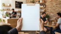Hands holding blank clipboard in busy cafe with customers and staff in background, suitable for menu design, restaurant branding, and hospitality marketing.
