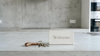 Welcome sign and keys on a concrete countertop in a modern minimalist interior, symbolizing new home, rental property, or hotel check-in.