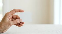 Mature adult male hand holding blank white business card on neutral background for corporate branding and professional marketing purposes.