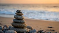 Balanced stone cairn on sandy beach at sunset with gentle ocean waves creating peaceful zen meditation atmosphere for wellness and mindfulness practices.