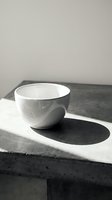 White ceramic bowl casting shadow on concrete surface in minimalist kitchen setting with natural lighting for modern home decor and tableware design.