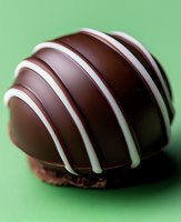Dark chocolate truffle with white stripes on green background, macro shot showing texture and glossy surface, sweet dessert confectionery detail.