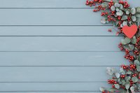 Red winter berries and eucalyptus leaves with heart decoration frame on rustic blue wooden background. Festive holiday border layout with copy space.