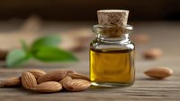 Natural almond oil in glass bottle with cork stopper surrounded by fresh almonds on wooden surface for skincare and aromatherapy treatments.
