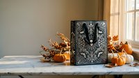 Ornate black tarot card with mystical symbols displayed on rustic wooden table surrounded by autumn pumpkins and dried branches in cozy interior setting.