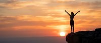 Woman silhouette with raised arms celebrating success on mountain cliff at golden sunset. Freedom, achievement, motivation concept for wellness and personal growth.