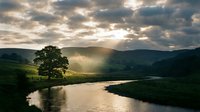 Scenic river landscape with dramatic sunlight breaking through clouds over rolling green hills and distant mountains, suitable for nature, travel, and environmental design projects.