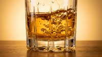Golden whiskey splashing in crystal tumbler glass on wooden surface with warm lighting for luxury beverage advertising and bar concepts.