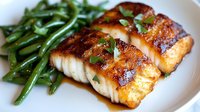 Seared white fish fillet with golden crust served alongside roasted green beans on white plate, ready for fine dining or cookbook use.