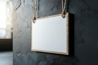 Blank wooden frame hanging on textured dark wall with rope. Empty white canvas in natural wood border creates minimalist composition against concrete surface.