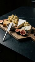 Gourmet cheese board with white grapes, fresh figs, and assorted cheeses on wooden serving platter. Ideal for food styling, culinary content, entertaining, and restaurant menus.