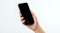 Hand holding black smartphone with blank screen against white background for mockup and app presentation designs.