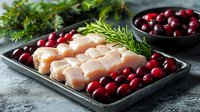 Raw chicken breast fillet pieces with fresh cranberries and rosemary sprigs on dark metal tray, healthy cooking ingredients on concrete background.