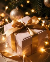 Elegant gift box with golden ribbon bow under Christmas tree with warm bokeh lights and ornaments creating festive holiday atmosphere for seasonal celebrations.