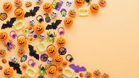 Halloween decorations with pumpkins, bats, spiders and candy scattered on orange background with copy space for seasonal party design and marketing materials.