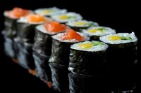Fresh sushi rolls with salmon and cucumber arranged in row on black background, traditional Japanese cuisine with nori seaweed wrap and rice.