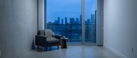 Modern empty apartment interior with floor-to-ceiling windows overlooking city skyline at dusk, featuring minimalist furniture and polished concrete flooring for contemporary home design.