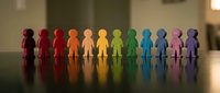 Colorful wooden figures standing in rainbow formation representing diversity, inclusion, teamwork and unity in workplace or community settings.